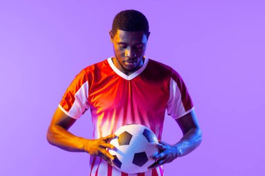 African american male soccer player with football over neon pink lighting. Sport, movement, training and active lifestyle concept.