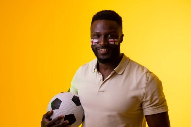 Image of happy african american male soccer fan with flag of england in yellow lighting. Sport, fans, cheering and emotions concept.
