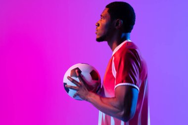 African american male soccer player with football over neon pink lighting. Sport, movement, training and active lifestyle concept.