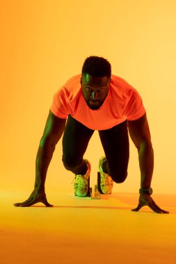 Vertical image of african american male athlete preparing for run in yellow lighting. Sport, movement, fitness and active lifestyle concept.