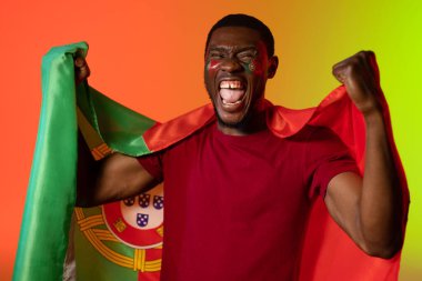 Portakal rengi ışıkta Portekiz bayrağı taşıyan Afro-Amerikan erkek futbol taraftarı portresi. Spor, hareket, eğitim ve aktif yaşam tarzı kavramı.
