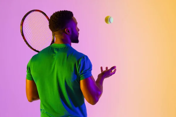 Image of back view of african american male tennis player in violet and yellow neon lighting. Sport, movement, fitness and active lifestyle concept.
