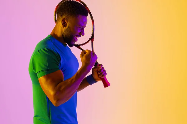 Image of successful african american male tennis player in violet and yellow lighting. Sport, movement, fitness and active lifestyle concept.