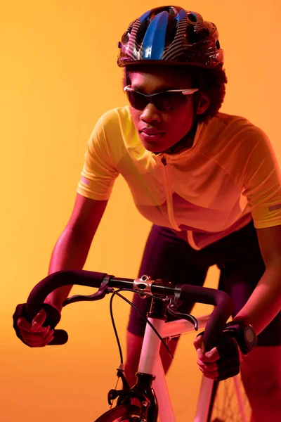 Κάθετη Εικόνα Του Αφροαμερικανού Ποδηλάτη Ιππασία Ποδήλατο Νέον Πορτοκαλί Φωτισμό — Φωτογραφία Αρχείου