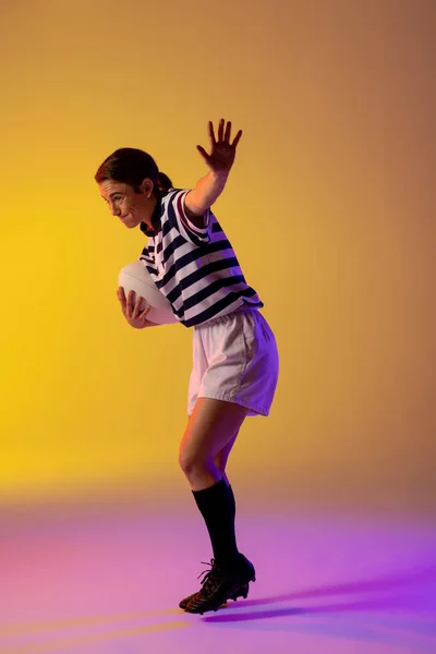 Caucasian female rugby player with rugby ball over neon pink lighting. Sport, movement, training and active lifestyle concept.