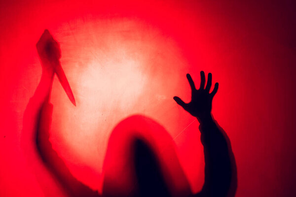 Composition of silhouette of woman holding knife on red background. Halloween tradition and celebration concept.