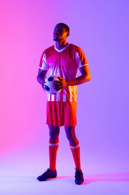 African american male soccer player with football over neon pink lighting. Sport, movement, training and active lifestyle concept.