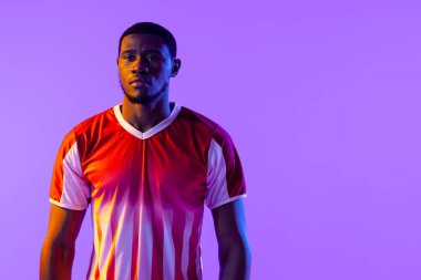 Portrait of african american male soccer player over neon pink lighting. Sport, movement, training and active lifestyle concept.