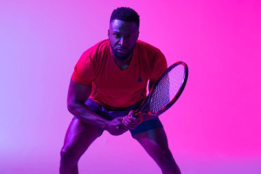 Image of african american male tennis player in neon pink lighting. Sport, movement, fitness and active lifestyle concept.