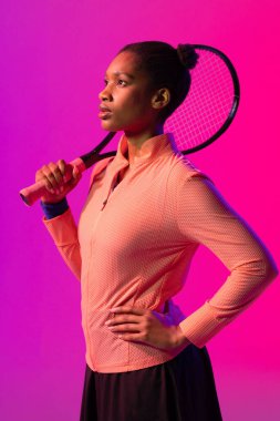 Mor ve pembe neon ışıklı Afro-Amerikan bayan tenis oyuncusunun dikey görüntüsü. Spor, hareket, fitness ve aktif yaşam tarzı konsepti.