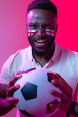 Vertical image of african american male soccer fan with flag of england in neon pink lighting. Sport, fans, cheering and emotions concept.