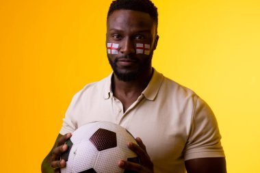 Image of african american male soccer fan with flag of england in yellow lighting. Sport, fans, cheering and emotions concept.