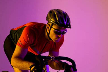 Caucasian male cyclist with bicycle over pink lighting. Sport, movement, training and active lifestyle concept.