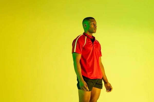 African american male rugby player over yellow lighting. Sport, movement, training and active lifestyle concept.