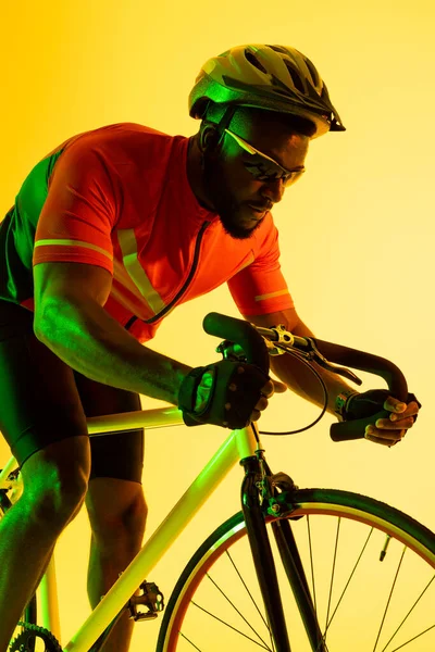 Vertical image of african american male cyclist riding bike in yellow lighting. Sport, movement, fitness and active lifestyle concept.