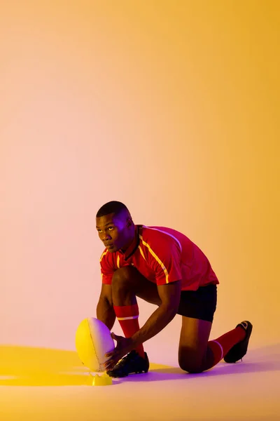 African American Male Rugby Player Crouching Rugby Ball Pink Lighting — ストック写真