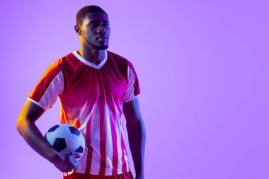 African american male soccer player with football over neon pink lighting. Sport, movement, training and active lifestyle concept.