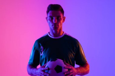 Beyaz erkek futbolcunun portresi neon pembe ışıkta futbol oynuyor. Spor, hareket, eğitim ve aktif yaşam tarzı kavramı.