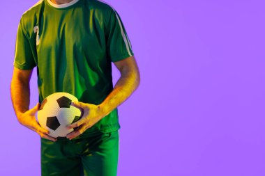 Caucasian male soccer player with football over neon pink lighting. Sport, movement, training and active lifestyle concept.