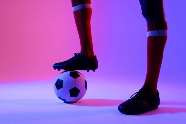 African american male soccer player with football over neon pink lighting. Sport, movement, training and active lifestyle concept.
