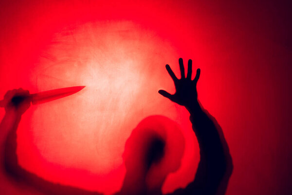 Composition of silhouette of man holding knife on red background. Halloween tradition and celebration concept.