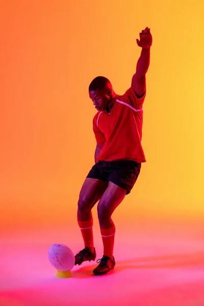 Jugador Rugby Masculino Afroamericano Pateando Pelota Rugby Sobre Iluminación Rosa — Foto de Stock