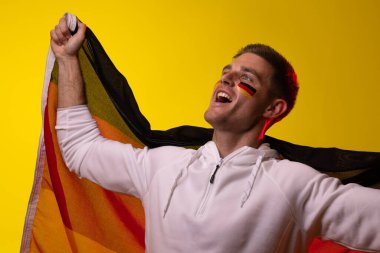 Sarı ışıkta Almanya bayrağı taşıyan mutlu beyaz erkek futbol taraftarı. Spor, hareket, eğitim ve aktif yaşam tarzı kavramı.