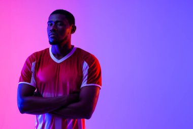 Portrait of african american male soccer player over neon pink lighting. Sport, movement, training and active lifestyle concept.