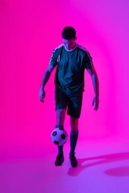 Beyaz erkek futbolcu, neon pembe ışıkta topu tekmeliyor. Spor, hareket, eğitim ve aktif yaşam tarzı kavramı.