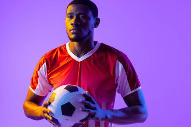 African american male soccer player with football over neon pink lighting. Sport, movement, training and active lifestyle concept.