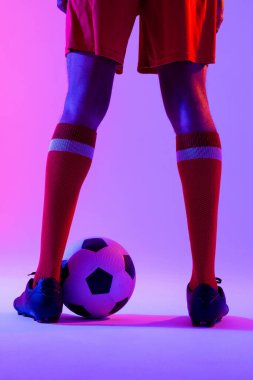 African american male soccer player with football over neon pink lighting. Sport, movement, training and active lifestyle concept.