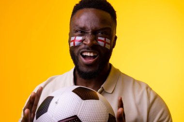 Image of african american male soccer fan with flag of england cheering in yellow lighting. Sport, fans, cheering and emotions concept.
