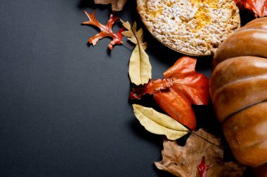 Balkabağı bileşimi, renkli sonbahar yaprakları ve siyah arkaplanda turta. Cadılar Bayramı, sonbahar, gelenek ve kutlama konsepti.