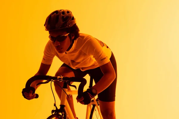 Image of african american female cyclist riding bike in yellow lighting. Sport, movement, fitness and active lifestyle concept.