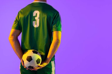 Caucasian male soccer player with football over neon pink lighting. Sport, movement, training and active lifestyle concept.