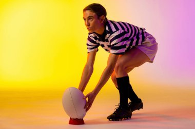 Beyaz kadın rugby oyuncusu, neon pembe ışıkta rugby topuyla çömeliyor. Spor, hareket, eğitim ve aktif yaşam tarzı kavramı.