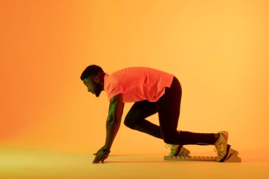 Sarı ışıkta koşmaya hazırlanan Afro-Amerikan erkek sporcunun görüntüsü. Spor, hareket, fitness ve aktif yaşam tarzı konsepti.
