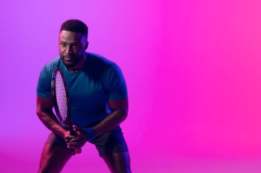 Image of focused african american male tennis player in neon pink lightning. Sport, movement, fitness and active lifestyle concept.
