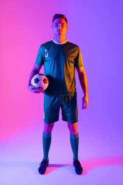 Beyaz erkek futbolcunun portresi neon pembe ışıkta futbol oynuyor. Spor, hareket, eğitim ve aktif yaşam tarzı kavramı.