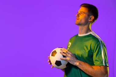 Caucasian male soccer player with football over neon pink lighting. Sport, movement, training and active lifestyle concept.