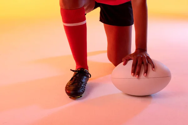 African american female rugby player with rugby ball over neon yellow lighting. Sport, movement, training and active lifestyle concept.