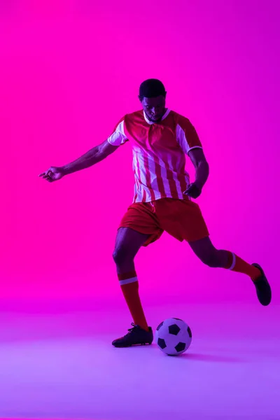 African American Male Soccer Player Kicking Football Neon Pink Lighting — Fotografia de Stock