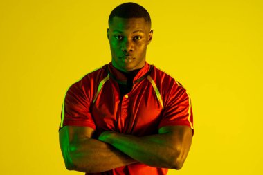 Portrait of african american male rugby player over yellow lighting. Sport, movement, training and active lifestyle concept.