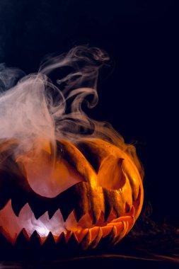 Siyah arka planda dumanlı balkabağı ve turuncu ışıklı Cadılar Bayramı kompozisyonu. Cadılar Bayramı geleneği ve kutlama konsepti.