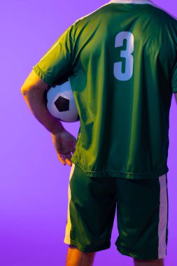 Caucasian male soccer player with football over neon pink lighting. Sport, movement, training and active lifestyle concept.