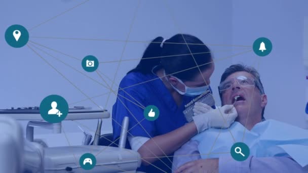 診療所で男性患者の歯を調べる白人女性歯科医の上のデジタルアイコンのネットワーク グローバルネットワークと医療技術の概念 — ストック動画