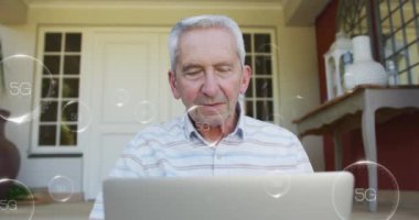 Animation of falling 5g icons over caucasian senior man using laptop. International day of older persons concept digitally generated video.