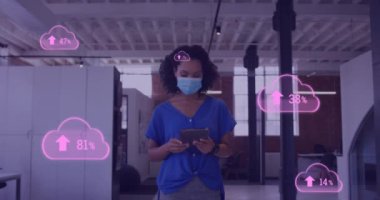 Animation of clouds with uploading over biracial female doctor in face mask. Health, medicine, cloud computing and data processing concept digitally generated video.