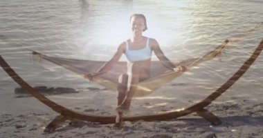 Animation of light over happy african american woman in hammock on beach. Holidays, vacations and relax concept digitally generated video.