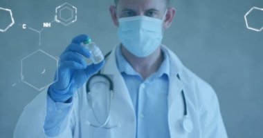 Animation of chemical structures over caucasian male doctor holding vaccine wearing face mask. Global covid 19 pandemic, medicine and healthcare services concept digitally generated video.